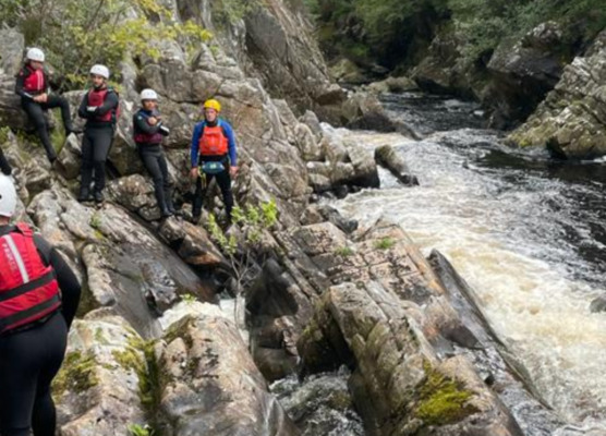 group clambering on rocks on the side of a river gorge